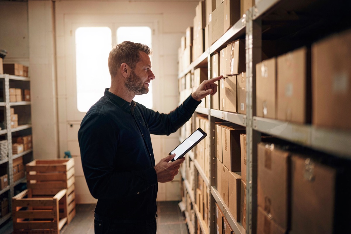 A shopkeeper checking stock against a tablet in the stockroom